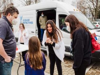 Center researcher Dr. Sahar Alameh and Center director Dr. Scott Berry talk to a grade school student and woman about environmental surveillance in front of the University of Kentucky’s Disease Detectives mobile lab van.